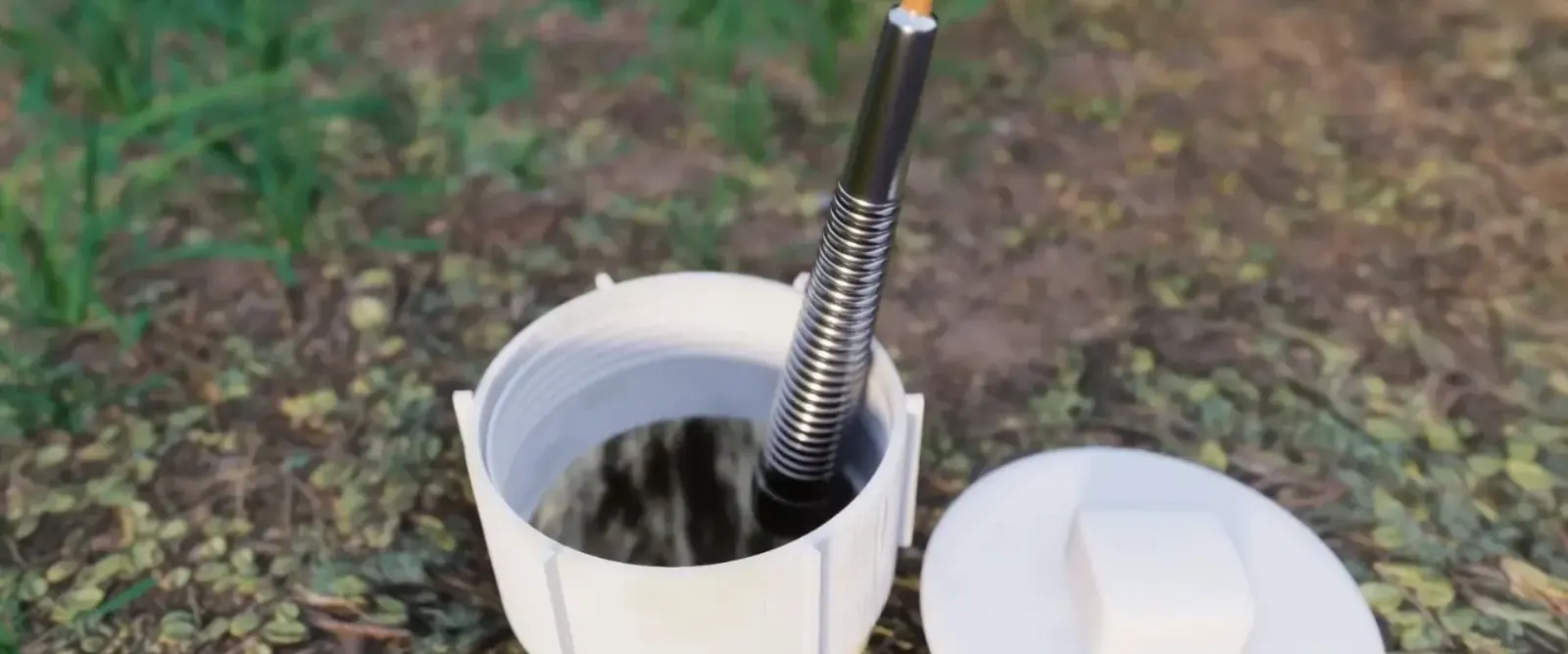 Camera cable entering an open sewer cleanout pipe in a lawn with the cap set beside it